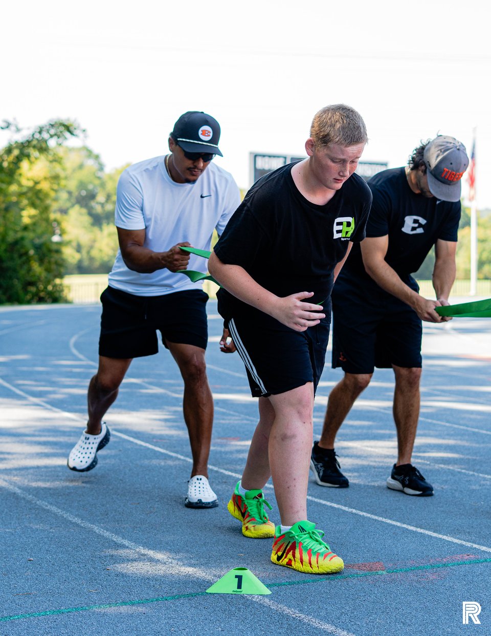 A coach leans in to guide athletes through their running posture on the outdoor track